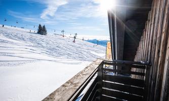 A snowy landscape with a ski slope and chairlifts in the background. The sun is shining brightly in the blue sky.