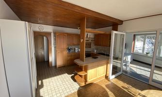 A bright kitchen with wooden cabinets and an open layout. The large windows let in plenty of daylight and connect the space with the outdoors.