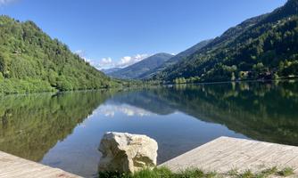 A quiet lake surrounded by green mountains. The sky is clear and reflects in the water.