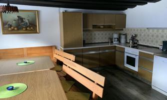 A modern kitchen with wooden shelves and a dining table. In the background, there is a picture of fruits hanging on the wall.