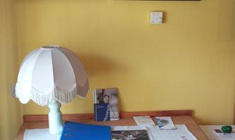 Desk with chair, table lamp and documents; above it two framed pictures on a yellow wall.