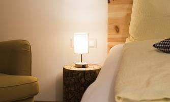A cozy bedroom with a modern nightstand and a warm lamp. A comfortable armchair completes the relaxed atmosphere.