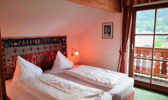 A cozy bedroom with two single beds and a wooden beam. The balcony offers a view of the surroundings, and the room has an inviting atmosphere.