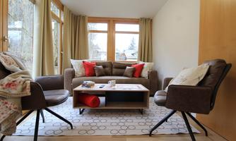 A cozy living room with a brown sofa and red cushions. Two chairs and a coffee table complete the inviting atmosphere.
