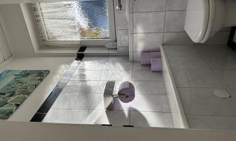 A modern bathroom with bright tiles and a toilet. In the background are purple towels and a window with natural light.
