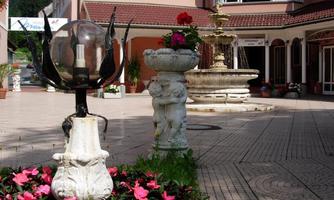 A beautiful courtyard with blooming flowers and an elegant fountain. In the foreground, there is a decorative lamp made of stone.