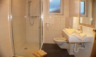 A modern bathroom with a glass shower and a sink. The walls are light tiled and the floor is dark.