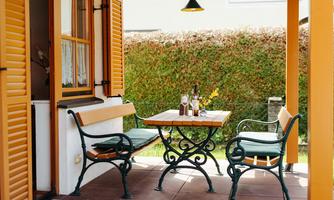 An inviting table with two chairs on a terrace. In the background, green shrubs and warm light can be seen.