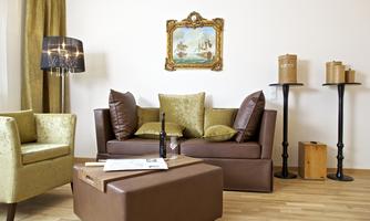 A stylishly furnished living room with a brown sofa and decorative cushions. In the background, there is a painting hanging, and there are some elegant pieces of furniture.