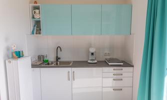 A modern kitchen with light blue upper cabinets and a gray countertop. On the work surface, there is a coffee machine and some kitchen utensils.