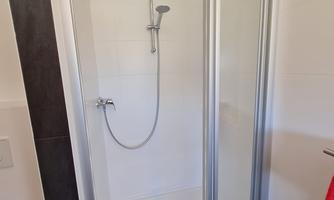 A modern shower with glass doors and a hand shower. A towel is lying on the floor.