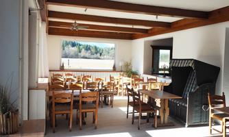 An inviting interior with wooden frames, tables, and chairs. Large windows provide plenty of daylight and a view of the greenery.