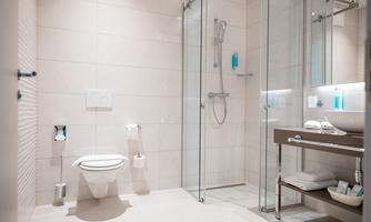 A modern bathroom with a glass shower and an elegant sink. The walls are tiled in light colors and there are some decorative toiletries.