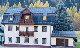 A charming two-story house with a red roof and a wooden balcony. Surrounded by trees in a rural setting.