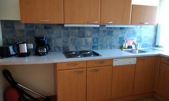 A modern kitchen with wooden cabinets and gray tiles. The equipment includes a stove, a sink, and kitchen appliances such as a kettle and a coffee machine.