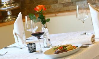 An elegantly set table with a dish, a glass of red wine, and a rose. In the background, water glasses and napkins can be seen.
