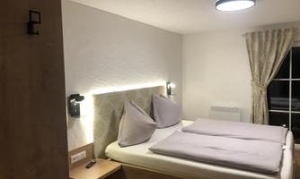 A cozy bedroom with a double bed and two pillows. The walls are light and the lighting is modern and pleasant.