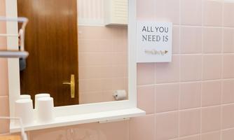 A bright bathroom with pink tiles and a white sink. On the wall hangs a sign that reads "ALL YOU NEED IS".