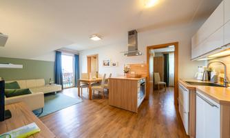 A modern kitchen with wooden details and a dining area. The living space is bright and inviting, featuring a sofa and a view of the surroundings.