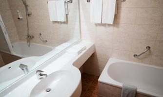 A modern bathroom with a sink, bathtub, and large mirrors. The walls are brightly tiled, and fresh towels are hanging.