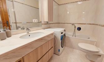 A modern bathroom with a bathtub, a sink, and a washing machine. The walls are tiled in light colors and the furniture is made of light wood.