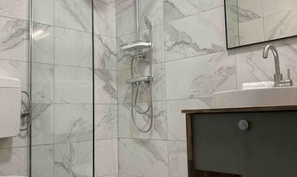 A modern bathroom with a splash-proof shower cubicle and elegant tiles. There is a sink with a wooden base and a mirror cabinet.