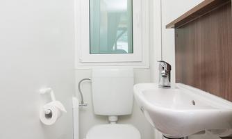 A small, modern bathroom with a toilet and a sink. There is a window that lets in natural light.