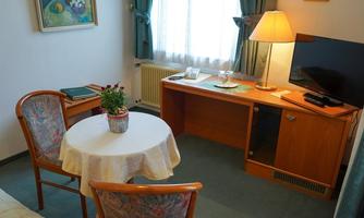 A cozy living area with a round table and two chairs. A television is on the desk, and the window lets in plenty of natural light.