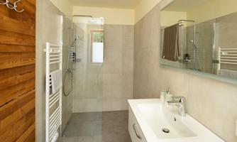 A modern bathroom with a glass-forged shower and a white sink. The walls are in neutral colors, and wooden details provide a warm accent.
