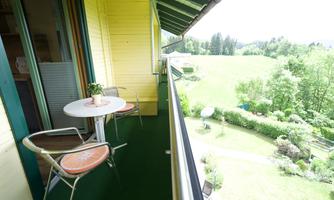 A cozy balcony with a table and chairs and a beautiful panoramic view. In the background, green meadows and trees can be seen.