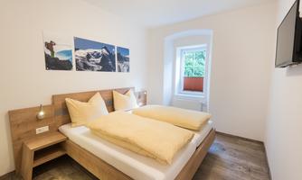 A modern bedroom with two beds and wooden furnishings. Large windows provide plenty of light and a cozy atmosphere.