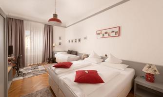 A bright room with two single beds and cozy decor. The room has large windows and a carpet for added comfort.