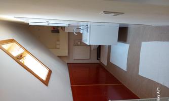 A bright bathroom with a sloping roof and a window. There is a sink with a cabinet and white mats on the floor.