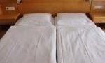 A simple hotel room with two single beds. The beds are made with white sheets and are positioned against a wall.