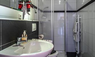 A modern bathroom with a shower, sink, and towels. The walls are tiled, and there is a pleasant lighting.