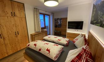 A cozy bedroom with wooden furniture and two beds decorated with red blankets. A window provides a view outside, and a television is mounted on the wall.