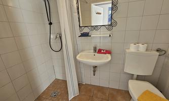 A modern bathroom with a shower cabin, a sink, and a toilet. The walls are tiled, and there are fresh towels as well as a mirror.