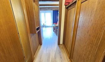 A bright hallway with wood paneling leads to a light-filled room. At the end of the hallway, large windows are visible.
