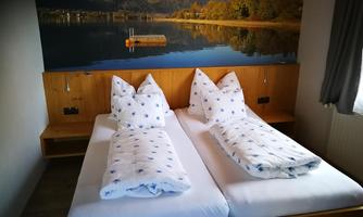 A cozy room with two single beds and comfortable pillows. In the background, there is a beautiful lake with a fjord landscape.