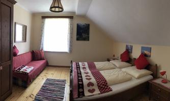 A cozy bedroom with two beds and red pillows. Next to the beds is a small table, and a window provides bright light.