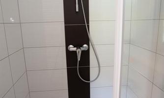 A modern shower enclosure with white tiles and a dark accent. The shower is equipped with a handheld showerhead and a fixed shower rod.