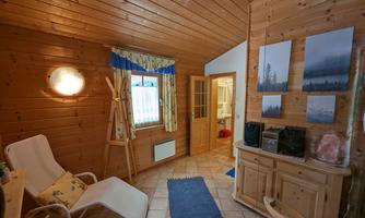 A cozy room with wooden paneling and warm lighting. There are chairs, a dresser, and pictures on the wall.