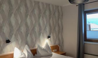 A modern bedroom with two beds and elegant decor. The walls are designed with a stylish pattern and a window lets in natural light.