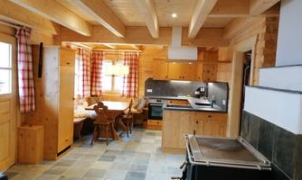A cozy wooden kitchen with a dining table and chairs. The windows are decorated with checked curtains.