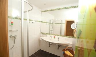 A modern bathroom with a shower and a sink. The walls are tiled white and there is a large mirror.