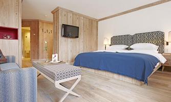 A modern room with wooden paneling and a large double bed. There is a flat-screen TV and a cozy seating area.