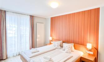 A cozy room with two single beds and a modern wooden design. Large windows provide plenty of daylight.