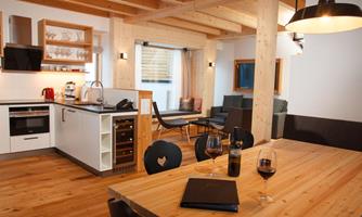 A modern, bright kitchen with a dining area and a cozy living space. Wooden floors and large windows create an inviting atmosphere.