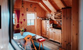 A cozy wooden cabin with rustic interior design. The table is lovingly set and there is a window front that lets in a lot of light.