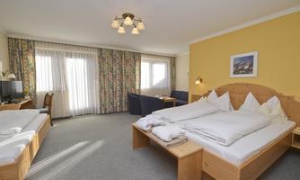 A cozy room with two beds, a sofa, and a table. Bright curtains and a warm color scheme create an inviting atmosphere.